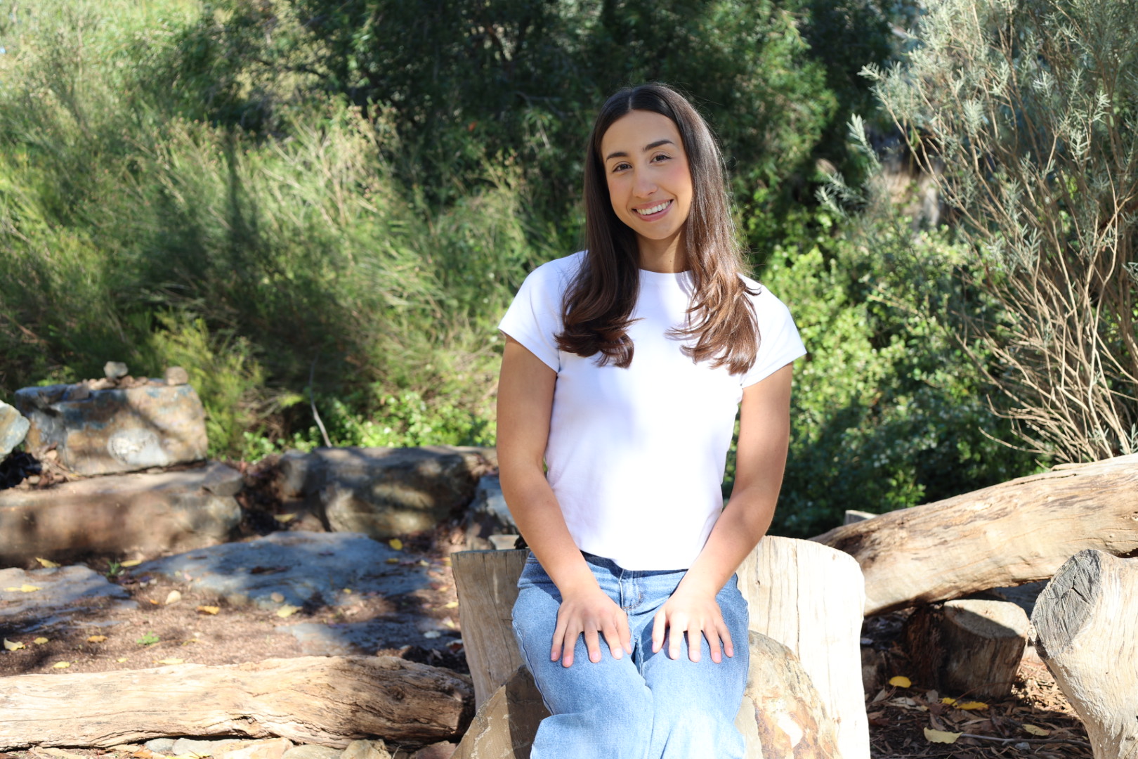 Tamsyn sitting on a log in a bush setting, smiling at the camera