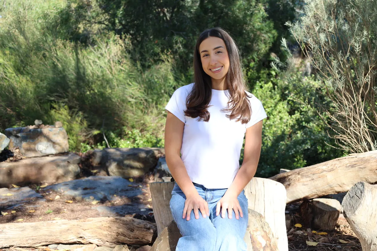Tamsyn sitting on a log in a bush setting, smiling at the camera